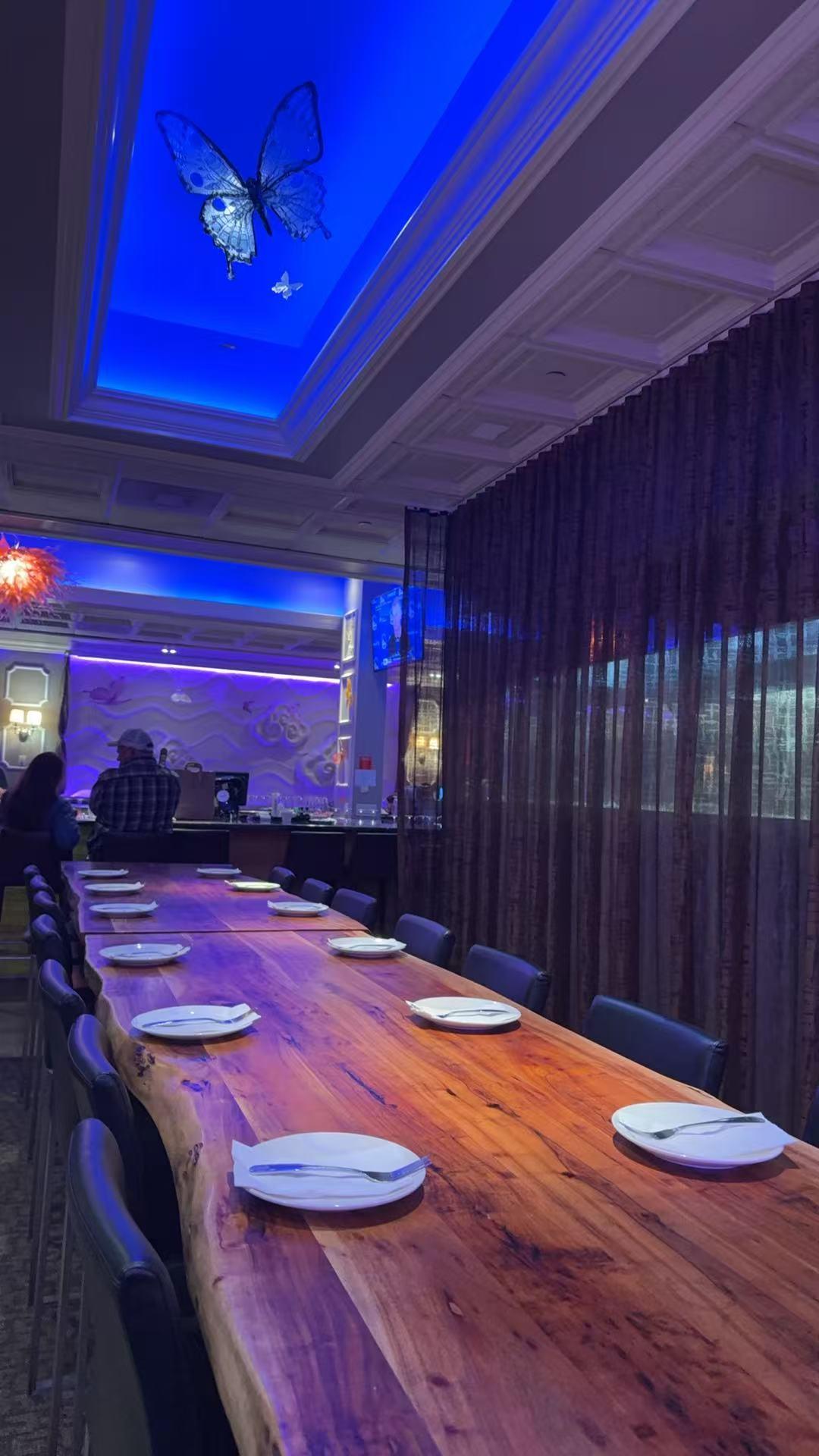 A long, rustic wooden table set for dining under a blue ceiling with a glowing butterfly light fixture.